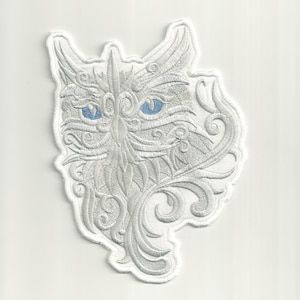 May include: White embroidered iron-on patch of an owl with blue eyes and intricate floral designs.