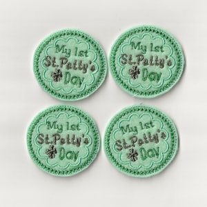 May include: Four green felt circles with white stitching around the edges. Each circle has a green shamrock and the text "My 1st St. Patty's Day" in silver thread.