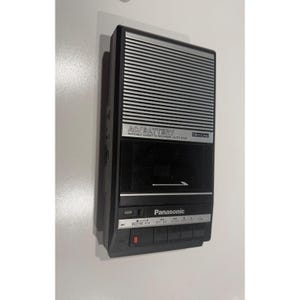 May include: A black and silver Panasonic portable cassette recorder featuring a Slim Line design, AC/Battery power options, and an auto stop function. The device includes a speaker grille, a cassette compartment, and control buttons.