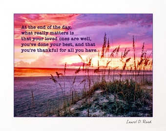 May include: A framed print featuring a beach scene at sunset. The sky transitions from pink to purple, with the ocean and sand in the foreground. Text reads: "At the end of the day, what really matters is that your loved ones are well..."