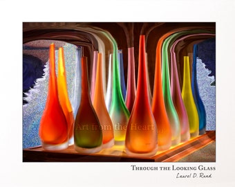 May include: A collection of colorful glass vases in various shades of red, orange, yellow, green, blue, and purple. The vases are arranged in a row on a wooden surface. The text "Art from the Heart" is visible in the image.