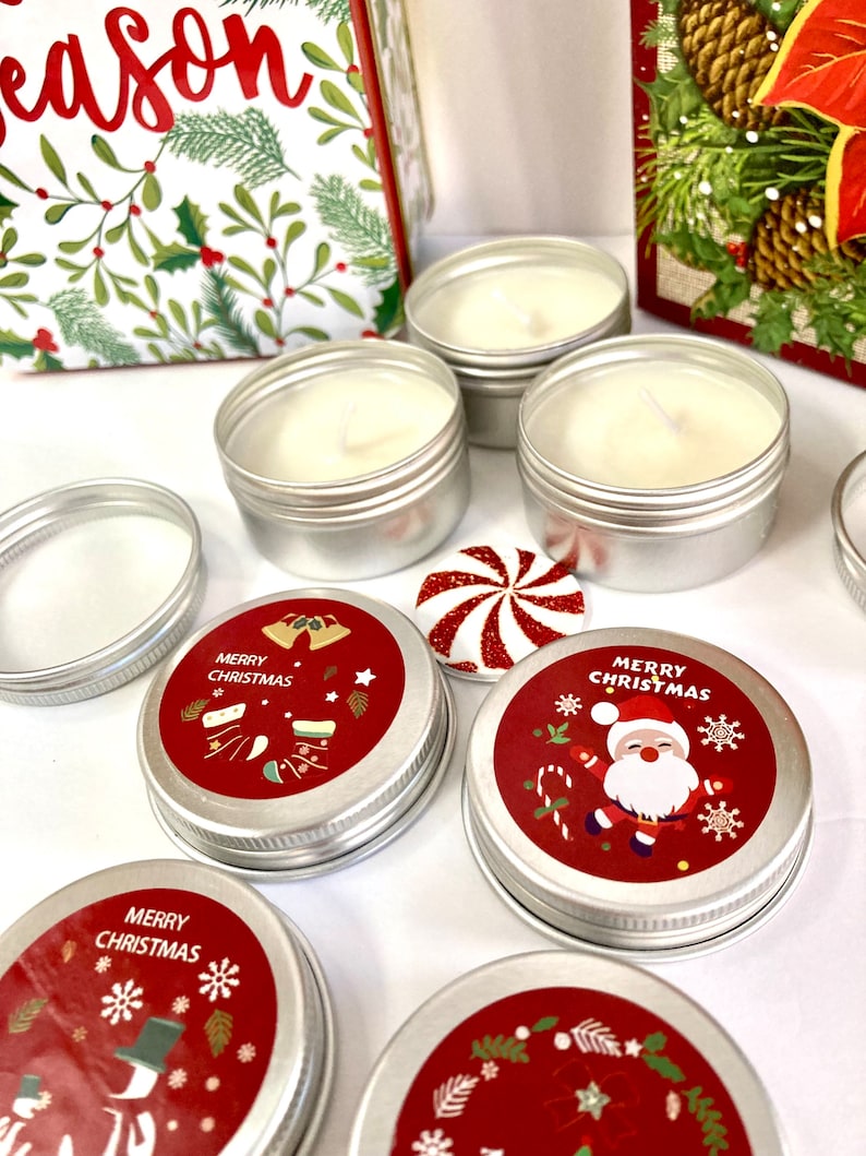 May include: Several small, silver candle tins filled with white wax and wicks. The lids are adorned with red labels displaying "Merry Christmas" and festive illustrations. A peppermint candy and a gift box with holly designs are also present.