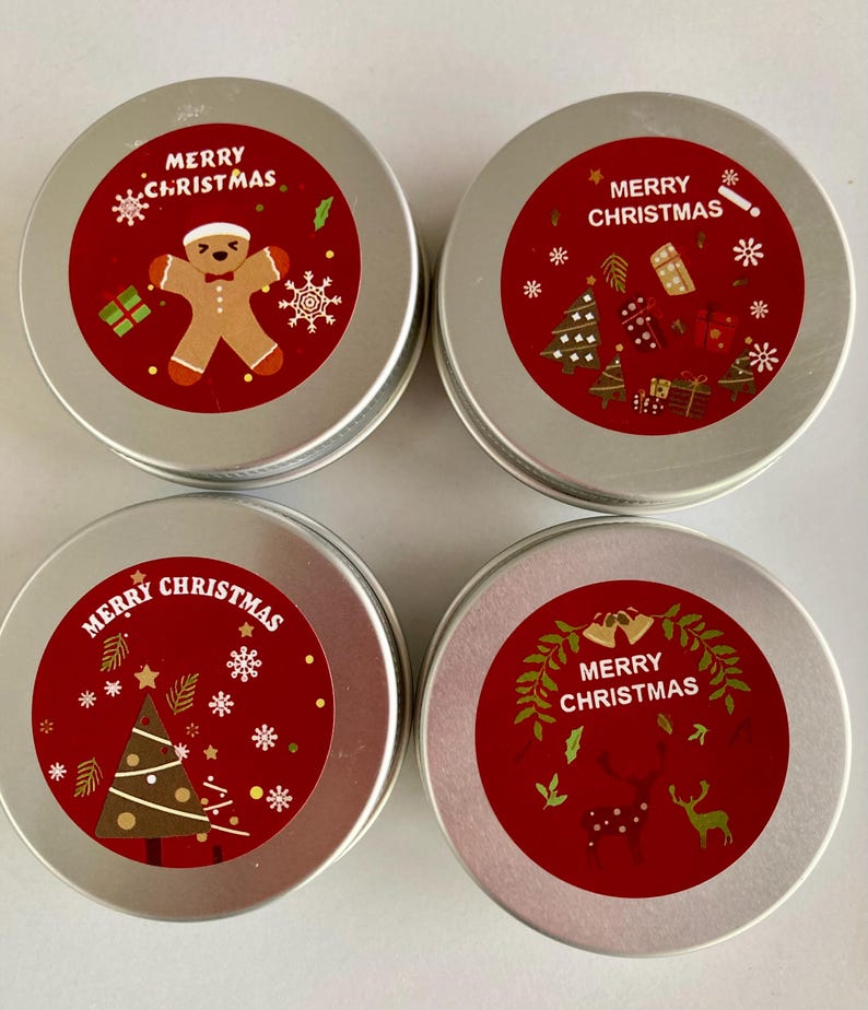 May include: Four small, round, silver tins with red labels. Each tin has "Merry Christmas" text and festive illustrations, including a gingerbread man, Christmas tree, and reindeer, ideal for gifting.