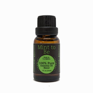 May include: A small amber glass bottle with a black cap and a label that reads "Mint to Be" with green accents. The label also says "Made by humblelove" and "100% Pure Essential Oil Blend" with a measurement of "0.5 fl. oz. (15ml)".