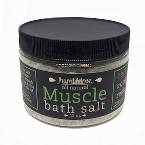 Puede incluir: Un tarro de vidrio con tapa negra lleno de sales de baño blancas. La etiqueta dice "humblelove all natural Muscle bath salt 12 oz".
