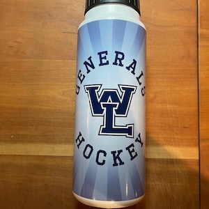 May include: White water bottle with a black cap. The bottle features the text "GENERALS HOCKEY" in navy blue, with a stylized "WL" logo. The background has a light blue radial design.