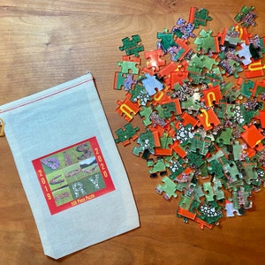 May include: A 108-piece jigsaw puzzle with scattered pieces in shades of green, red, and orange. A canvas bag with a red-bordered label displays the years 2019 and 2020, along with the text "DIS" and "PLAY". The bag is closed with a yellow drawstring.