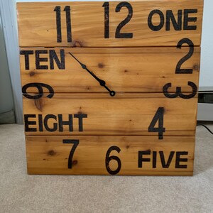 May include: A wooden clock with black painted numbers and hands. The numbers are written out, such as "ONE", "TWO", "TEN", and "EIGHT".