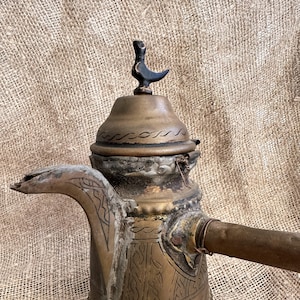 May include: An antique brass coffee pot with intricate engraved designs. The pot has a wooden handle and a decorative finial on the lid.
