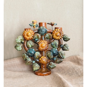 Peut inclure: Un candélabre en céramique brune présentant une structure en forme d'arbre ornée de fleurs sculptées orange et bleu sarcelle ainsi que de feuilles vertes. Deux petits oiseaux sont perchés sur les branches supérieures, sur une base circulaire.