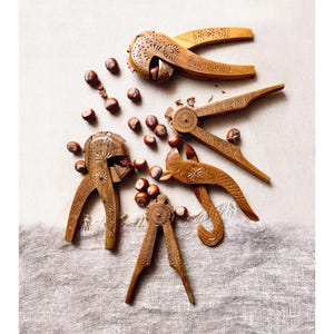 Könnte beinhalten: Draufsicht auf mehrere aufwendig geschnitzte Nussknacker aus Holz und verstreute Kastanien. Die Nussknacker in verschiedenen Größen und Designs weisen detaillierte Muster auf und sind auf einer strukturierten, hellen Oberfläche angeordnet.