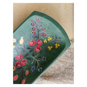 May include: A hand-painted, green wooden tray with a floral design. The tray features red roses, blue and yellow flowers, and berries. The flowers are painted on a dark green background.