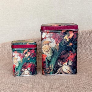 May include: Two rectangular metal storage tins of different heights, both featuring a dark, moody floral and butterfly print. The designs include white and yellow flowers, green foliage, and butterflies against a deep red and black background.