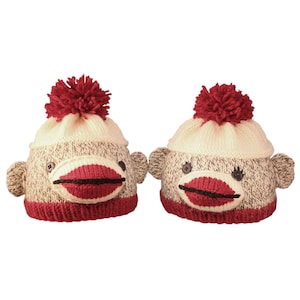 May include: Two knitted monkey hats with red pom-poms and red lips. The hats are beige and brown with black eyes.