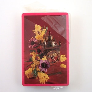 May include: A vintage clock with a gold finish and Roman numeral face, surrounded by yellow mimosa flowers and purple anemones on a red background.