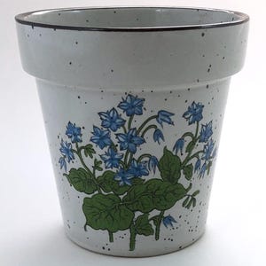 May include: A ceramic flower pot with a light gray speckled finish. The pot features a blue floral design with green leaves. The rim is outlined with a dark brown band. The pot is suitable for indoor or outdoor use.