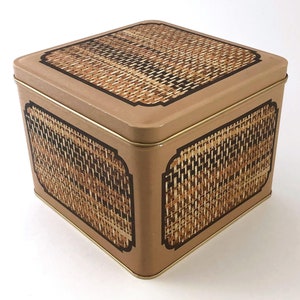 May include: A square, brown metal tin with a woven pattern on the lid and sides. The tin has a gold trim around the edges.