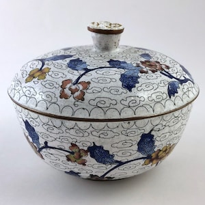 May include: A white ceramic bowl with a lid, decorated with a floral pattern in blue, yellow, and red. The bowl has a white background with a cloud-like pattern.