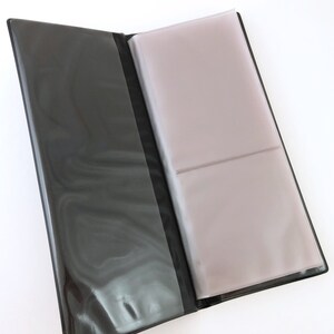 May include: Black photo album with clear plastic sleeves for holding photos. The album is open to reveal the empty sleeves.