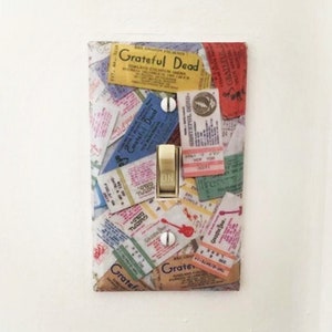 May include: A light switch cover with a collage of vintage Grateful Dead concert ticket stubs. The cover is white with a gold-colored light switch.