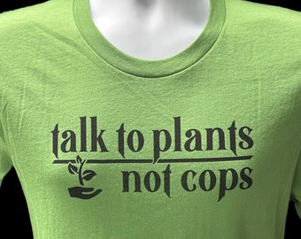 May include: A green t-shirt with the text "talk to plants not cops" in black lettering. A small plant icon is above the word "not".