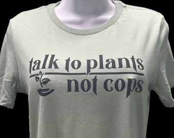 May include: A light green t-shirt with the text "talk to plants not cops" in dark blue lettering. A small plant icon is above the word "not".