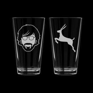 May include: Two clear glass pint glasses with white designs. One glass features a silhouette of a man with glasses and a beard. The other glass features a silhouette of a leaping antelope.