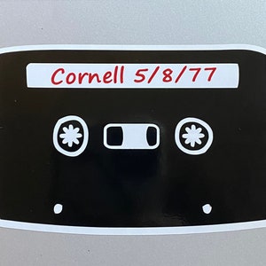 May include: A black and white cassette tape sticker with the text "Cornell 5/8/77" in red lettering.