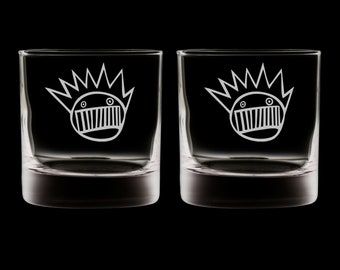 May include: Two clear glass tumblers with a white graphic of a cartoon face with a crown of spikes.