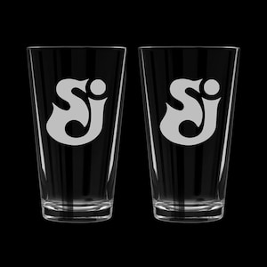 May include: Two clear glass pint glasses with the letters "SJ" etched on the front in a white, stylized font.