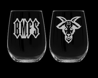 May include: Two clear glass wine glasses with etched designs. The left glass has the letters "RMFS" etched on it. The right glass has a goat head with the number "33" etched on its forehead.