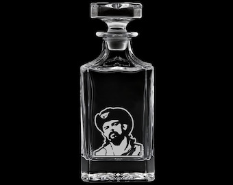 May include: A clear glass liquor decanter with a square body and a stopper. The decanter features a black and white portrait of a man wearing a cowboy hat. The background is black.