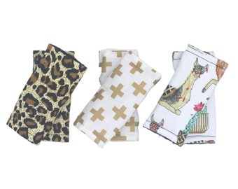 May include: Three fabric strap covers for car seats. One cover features a leopard print, another has a gold cross pattern, and the third has a white background with a llama and cactus design.