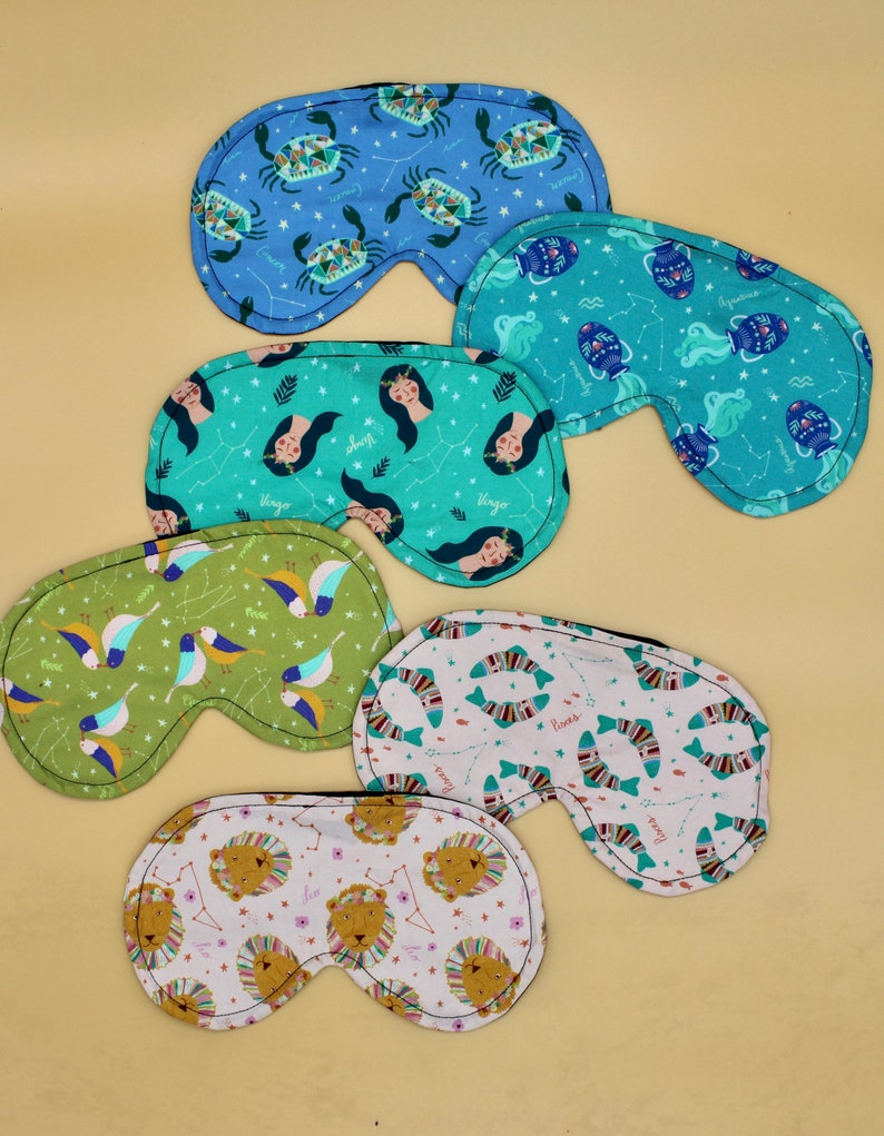 May include: Set of six zodiac-themed sleep masks. Each mask features a different zodiac sign with a colorful design. The signs include Cancer, Aquarius, Virgo, Pisces, Leo, and Gemini.