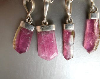 May include: Four raw, deep pink tourmaline crystal pendants, each set in a polished silver-toned metal cap with a matching bail. The crystals exhibit natural, irregular shapes with translucent edges and varying shades of magenta and dark pink.