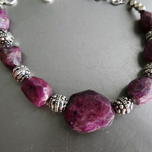 May include: A purple gemstone bracelet with silver beads. The bracelet is made of large, faceted gemstones and small, round beads.