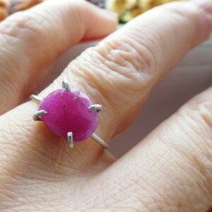 May include: A silver ring featuring a large, round, fuchsia-colored gemstone. The gemstone is held in place by four silver prongs. The ring is shown on a person's finger, with the background slightly blurred.