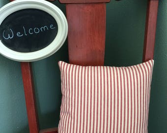 May include: A red wooden chair with a white framed chalkboard that says "Welcome" hanging on the back. A red and white striped pillow is sitting on the chair.