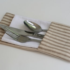 May include: A brown and white striped fabric napkin with a white napkin inside. A fork, knife, and spoon are placed on top of the white napkin.