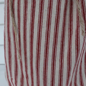 Puede incluir: Primer plano de una tela con un patr&oacute;n de rayas rojas y blancas. La tela tiene rayas verticales y una cuerda de fibra natural adjunta. La tela parece ser de estilo r&uacute;stico y campestre.