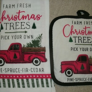 May include: A white Christmas-themed kitchen towel and pot holder set. The towel and pot holder feature a red truck carrying Christmas trees, with text that reads "Farm Fresh Christmas Trees Pick Your Own". The bottom of the towel has a red and green striped border.