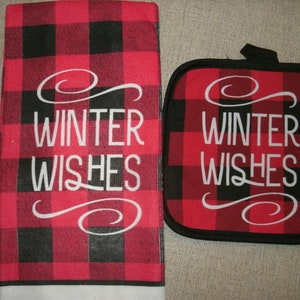 May include: A red and black buffalo plaid kitchen towel and pot holder set. The words "WINTER WISHES" are printed in white script on both items. The pot holder has a black border and a loop for hanging.