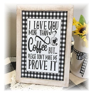 May include: A framed sign with a black and white gingham pattern border. The sign reads "I LOVE YOU MORE THAN Coffee BUT... PLEASE DON'T MAKE ME PROVE IT" in black lettering. A small coffee cup graphic is included.