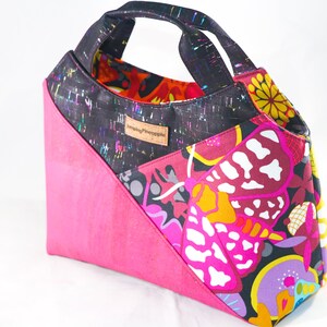May include: A black and pink tote bag with a colorful butterfly print and a black handle. The bag has a label that says "Sewing Pineapple".