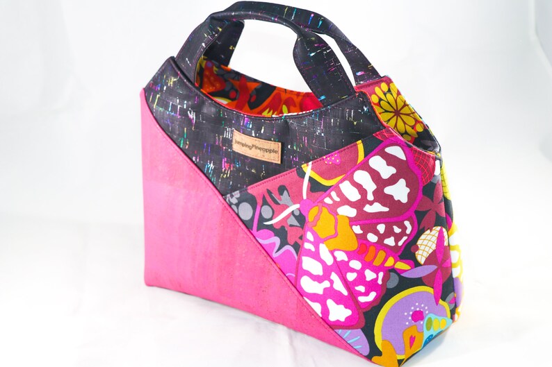 May include: A black and pink tote bag with a colorful butterfly print and a black handle. The bag has a label that says "Sewing Pineapple".