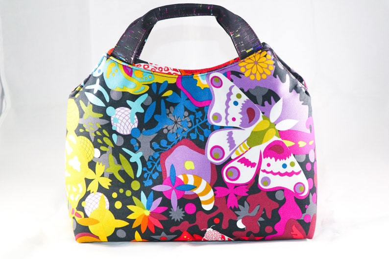 May include: A colorful tote bag with a black background and a butterfly pattern. The bag has a black handle and is made of fabric.