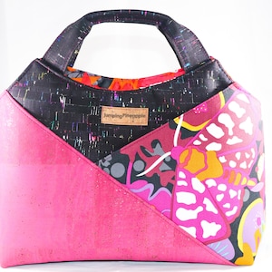 May include: A black, pink, and multi-colored tote bag with a cork bottom and a fabric handle. The bag has a geometric design with a butterfly pattern and the text "Jumping Pineapple" on the front.