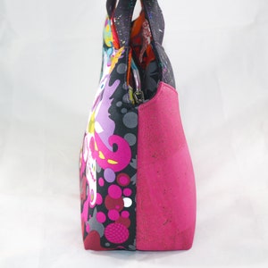 May include: A pink and black patterned tote bag with a pink cork bottom. The bag has a zipper closure and two top handles.