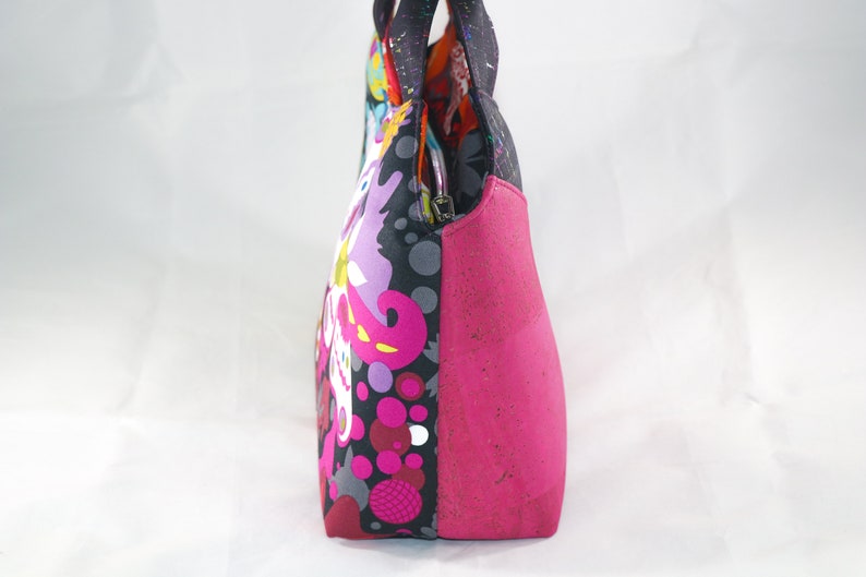 May include: A pink and black patterned tote bag with a pink cork bottom. The bag has a zipper closure and two top handles.