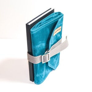 May include: A teal blue canvas notebook with a grey strap and buckle closure. The notebook is wrapped around a black hardback journal.